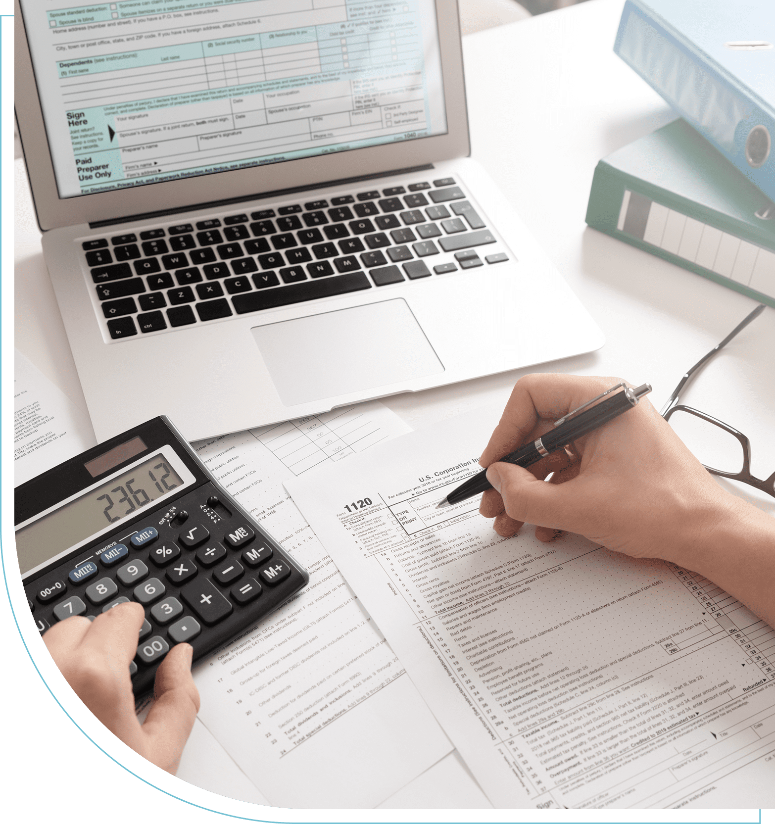 Group 4 (5) Person filling out tax forms with a pen, using a calculator and a laptop, with documents and folders on the desk.